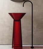 Red glass sink with black faucet against a beige wall