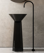 Black freestanding sink with curved faucet against a textured wall.