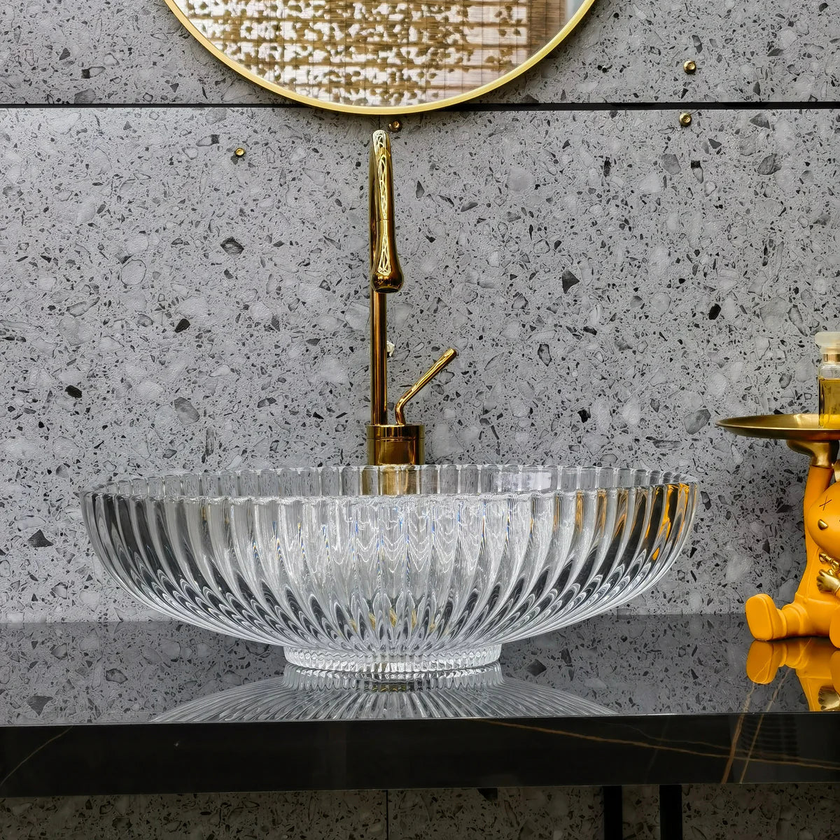 Bathroom vanity with crystal sink and gold faucet against a gray concrete wall.
